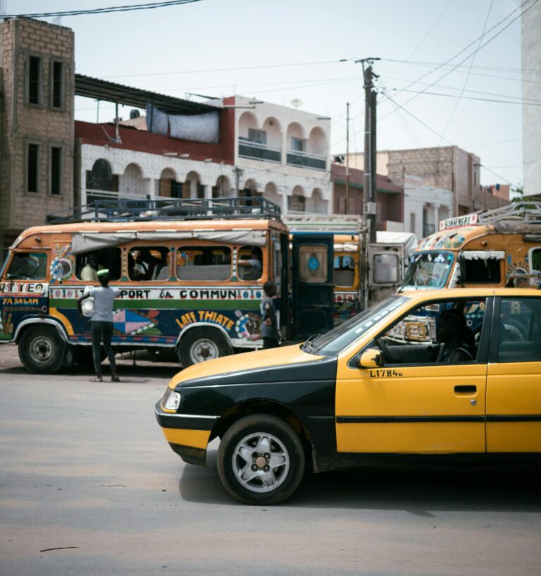 City street scene showing colorful buses and a yellow taxi, capturing urban life.