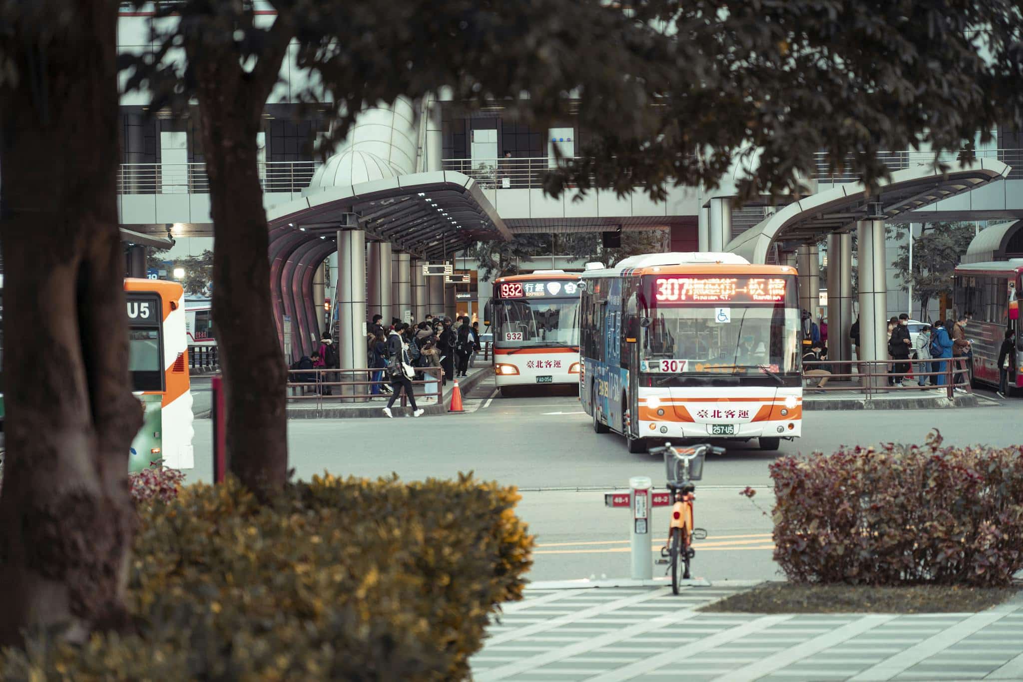 Crowded bus station with multiple buses and commuters in an urban setting.